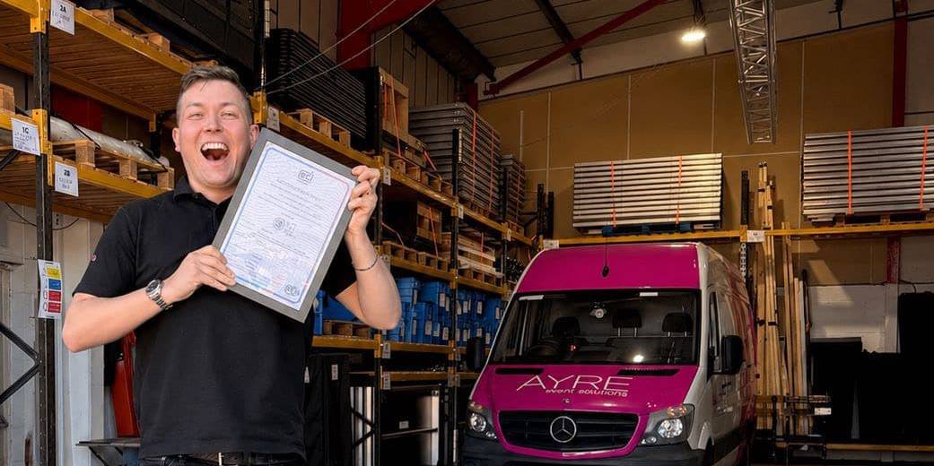 Ryan Driver-Ayre holding AYRE Event Solutions ISO9001 certification at the company warehouse
